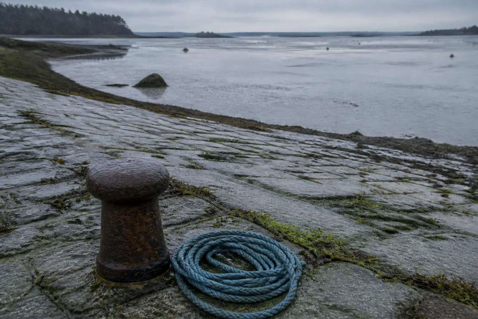 Un embarcadère de granit désert face à la mer basse, une bitte d'amarrage et des cordages enroulés