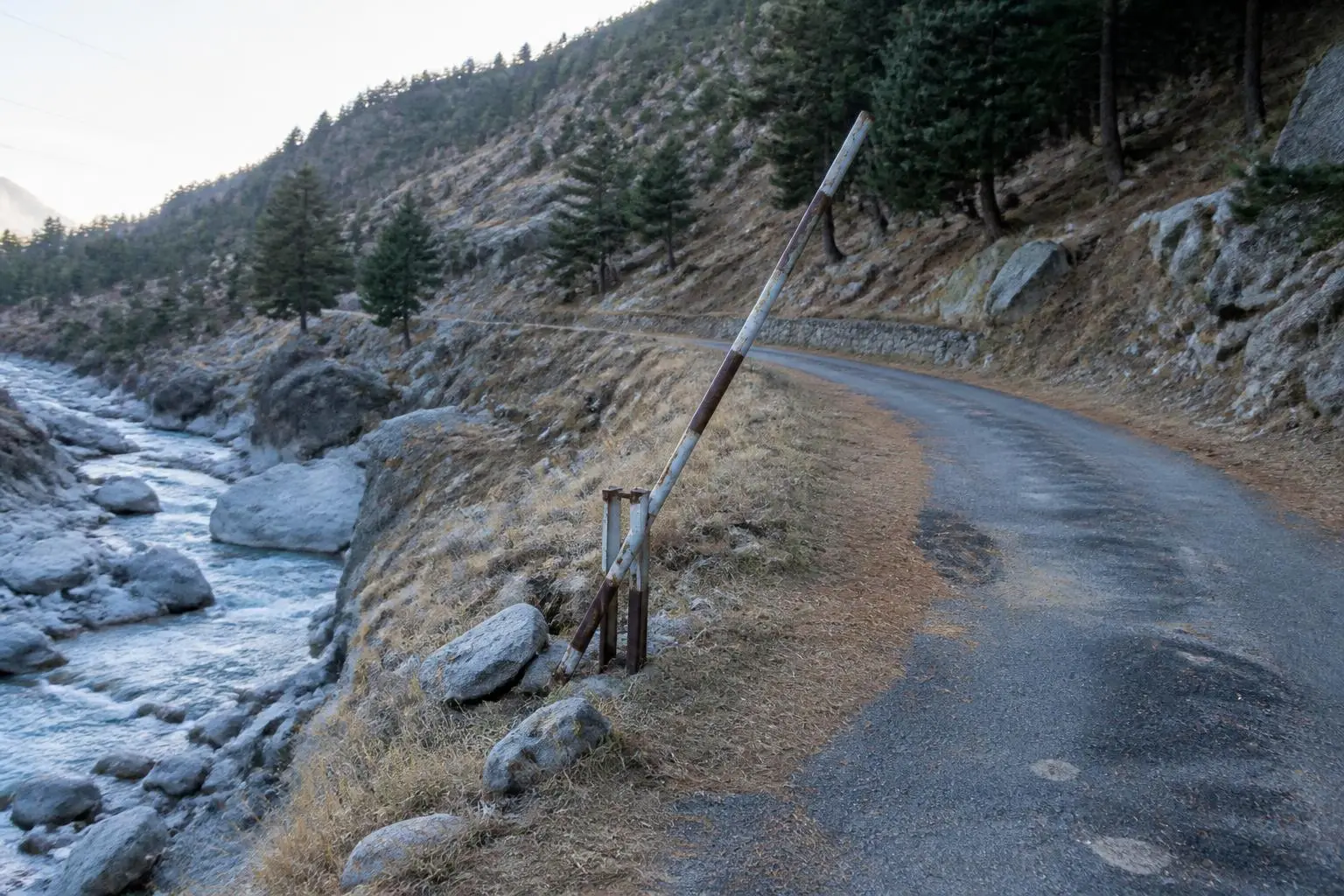 Une route de montagne étroite longeant un torrent, barrière métallique relevée contre le talus et pierriers de granit gris